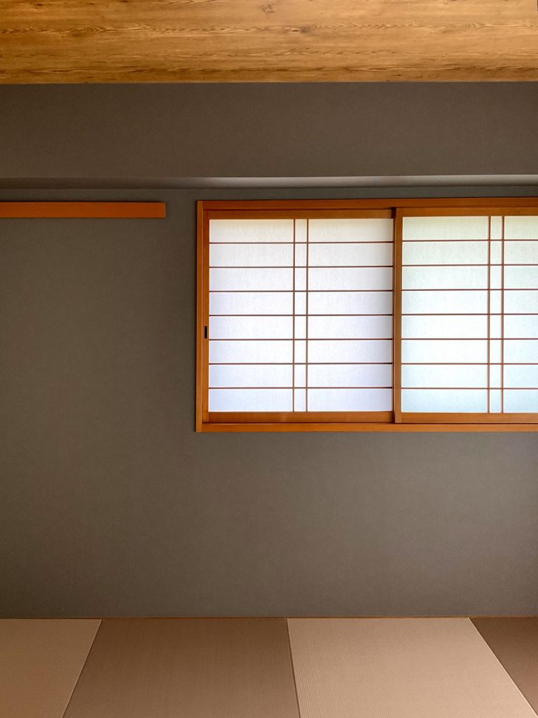 神戸市東灘区で施工した和室のリフォーム事例。木の質感を生かした印象的な天井に、ダークカラーのモルタル風の壁とモカカラーの半畳畳を組み合わせで、上品さとワイルドさが心地よく調和した空間に。