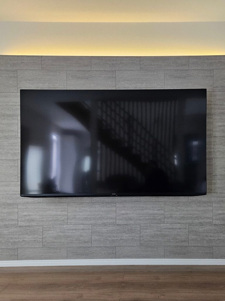 神戸市西区で施工した壁掛けテレビの造作壁リフォーム事例。間接照明とタイル柄のクロスで空間にアクセントをプラス。壁の裏側には収納スペースも確保し、デザインと機能性を両立したリビング空間です。